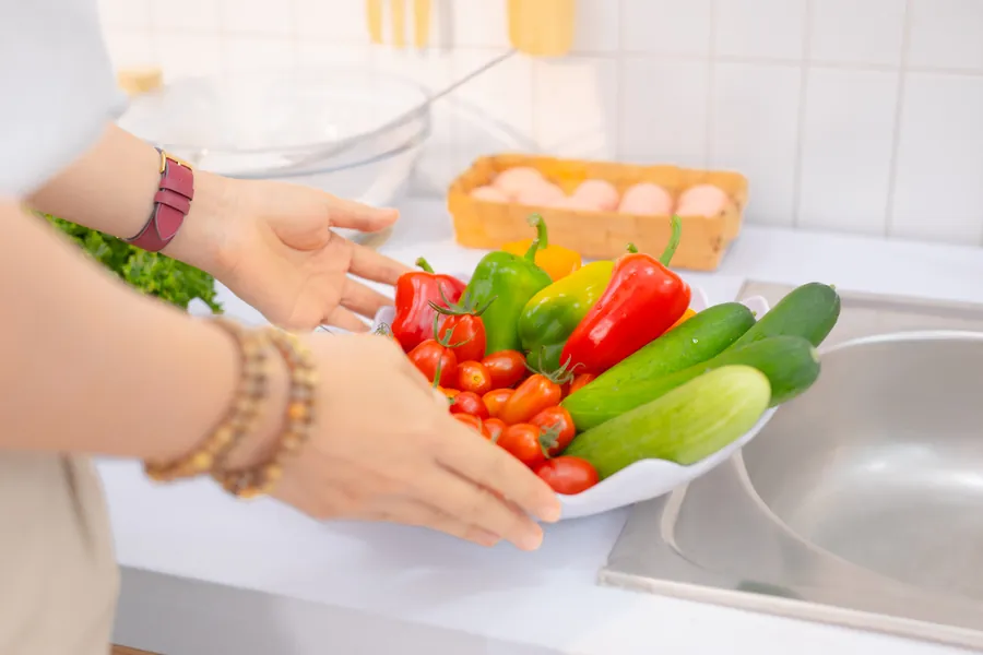 Đôi tay rửa rau củ tươi dưới vòi nước
